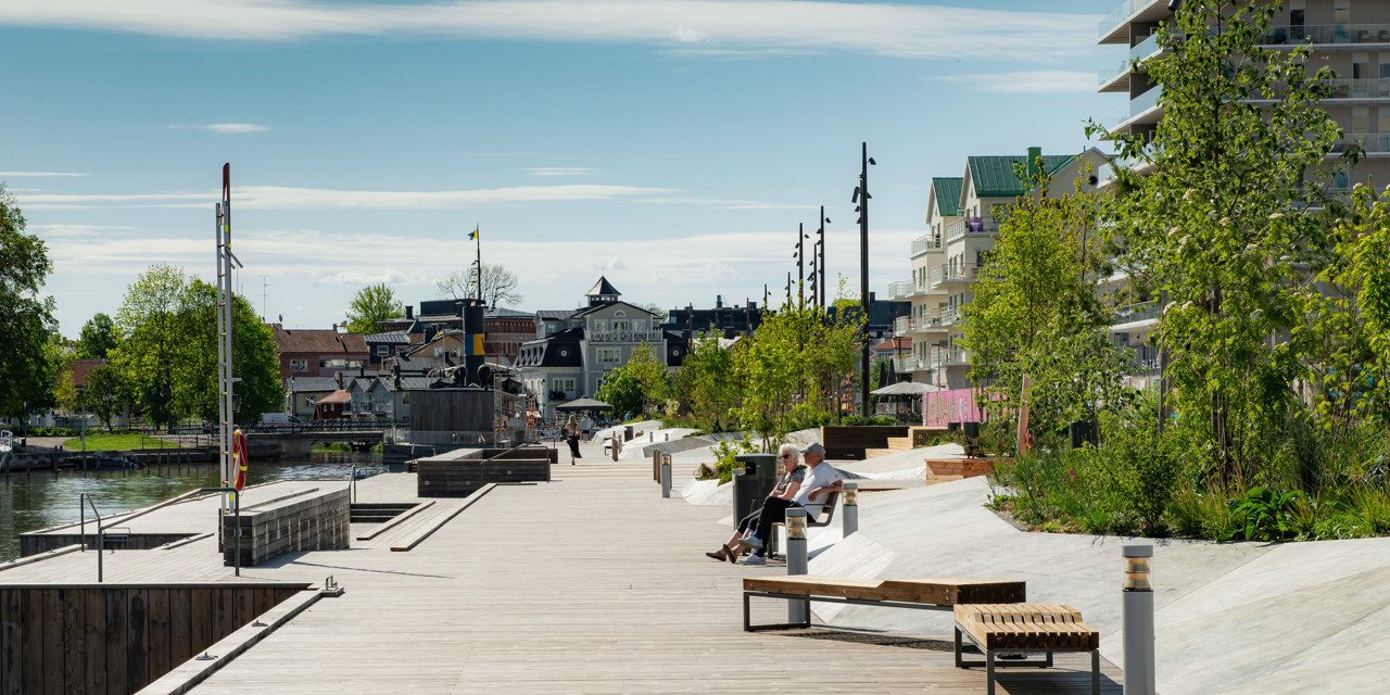 Några personer sitter på en bänk vid en kaj. 
