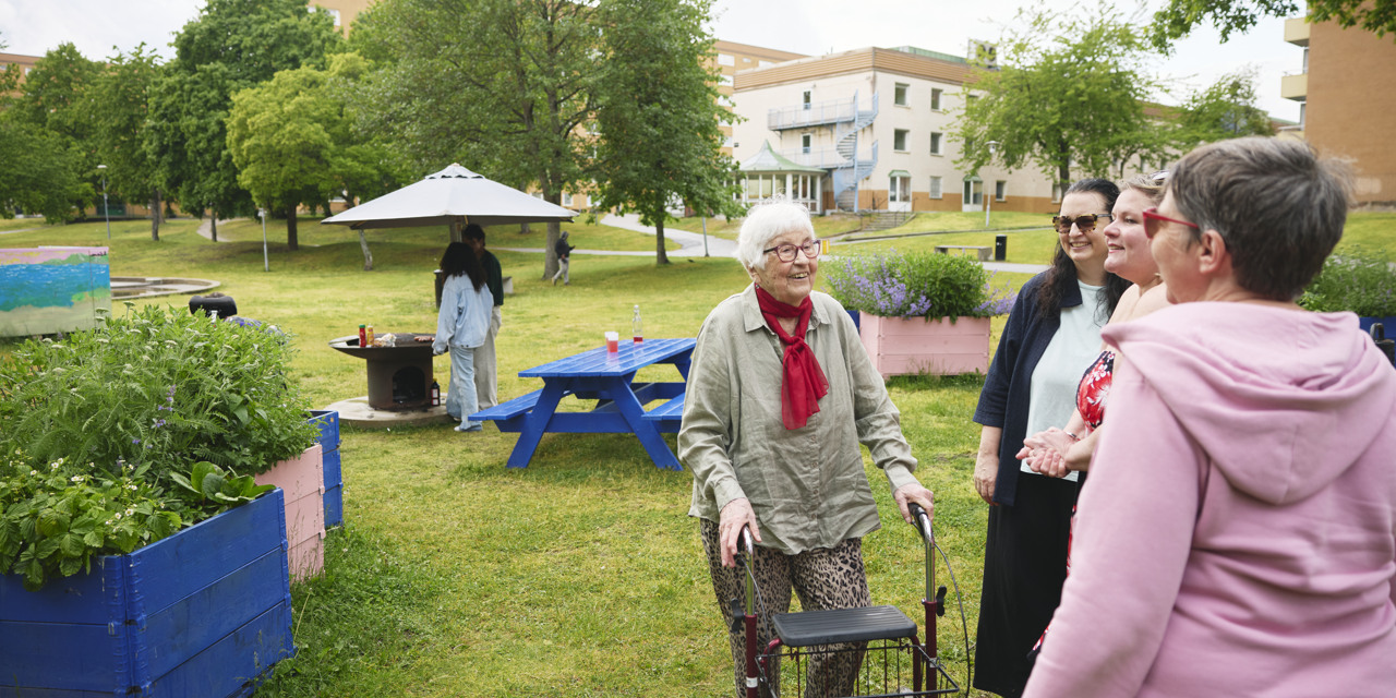 Personer samtalar och skrattar på en grönskande innergård i ett bostadsområde.