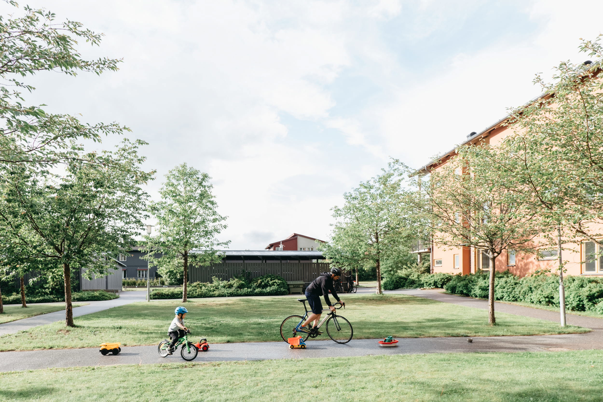 En pappa och ett barn cyklar slalom på en innergård.