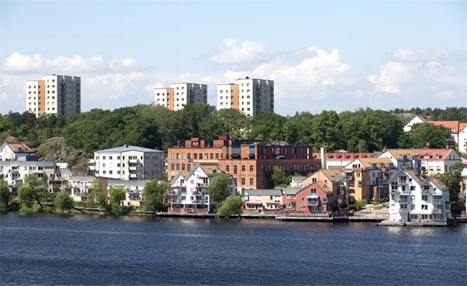 Flerbostadshus i olika storlekar och höjder samt skogspartier som finns bakom en vattenlinje.