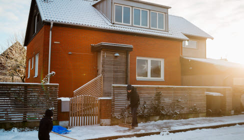 Hus i vintersol, barn som skottar snö utanför.