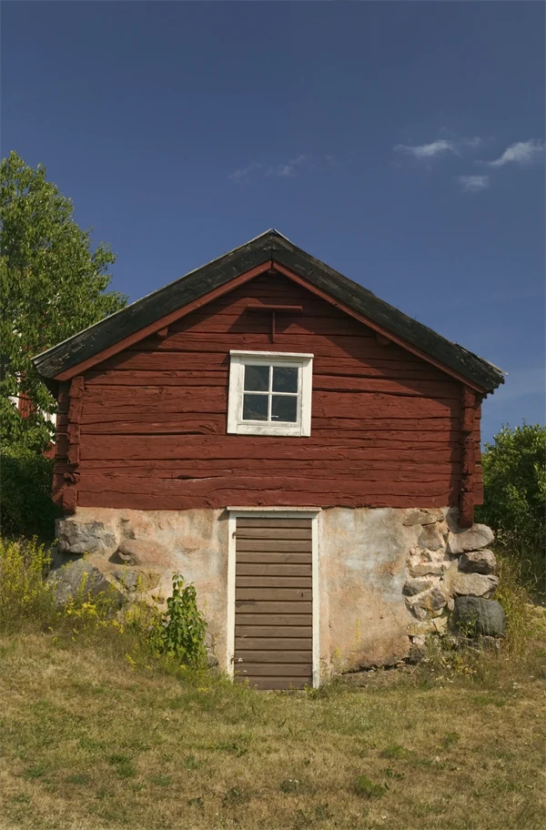 Röd stuga med en äldre källarvägg av sten