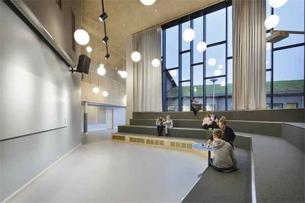 En samlingslokal med tygklädda gradänger i fyra nivåer och barn som sitter och spelar spel eller läser för sig själva.