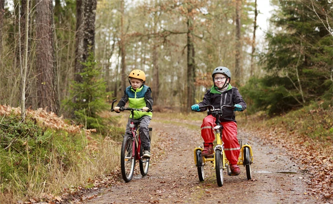 Två barn i regnkläder som cyklar på en grusväg.