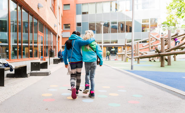 Två ungdomar med ryggen mot kameran går mot en skolbyggnad.