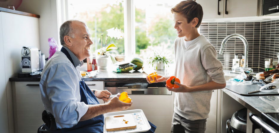 Pappa och son lagar mat i köket. Pappan använder rullstol. De är glada.