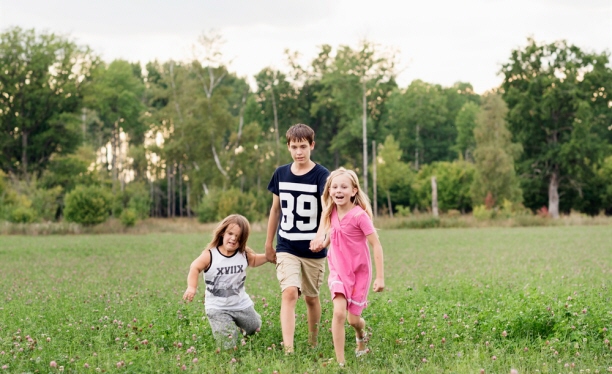 Tre barn som står i en gräsmatta/äng.
