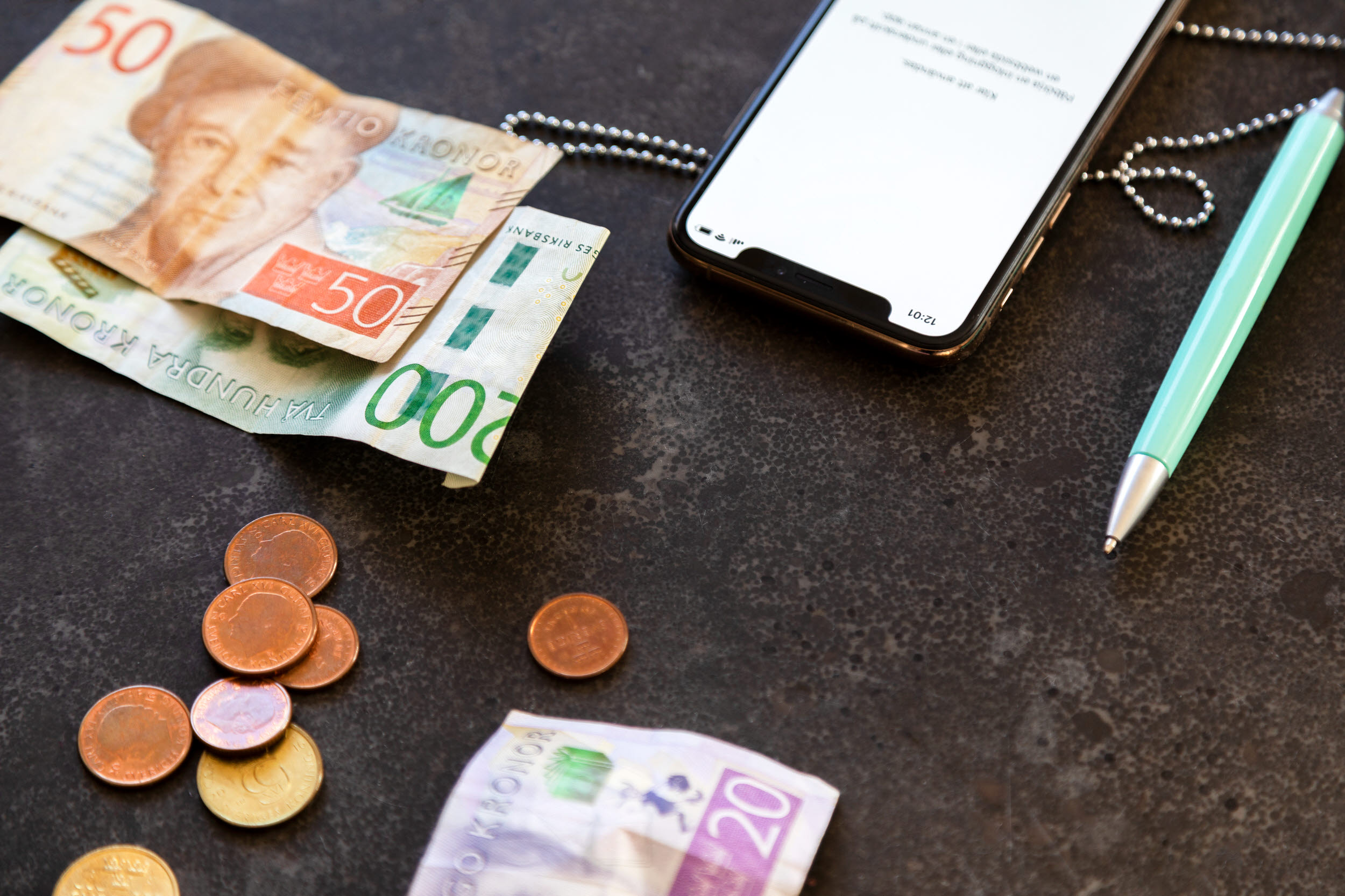 Pengar, telefon och en penna på ett bord.