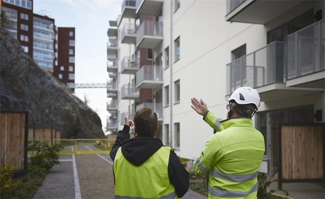 Två byggarbetare pekar och visar nybyggda flerbostadshus.