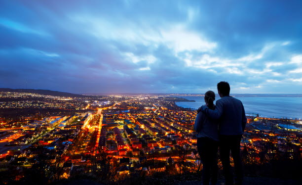 Två personer som tittar ut över upplyst stad från höjd