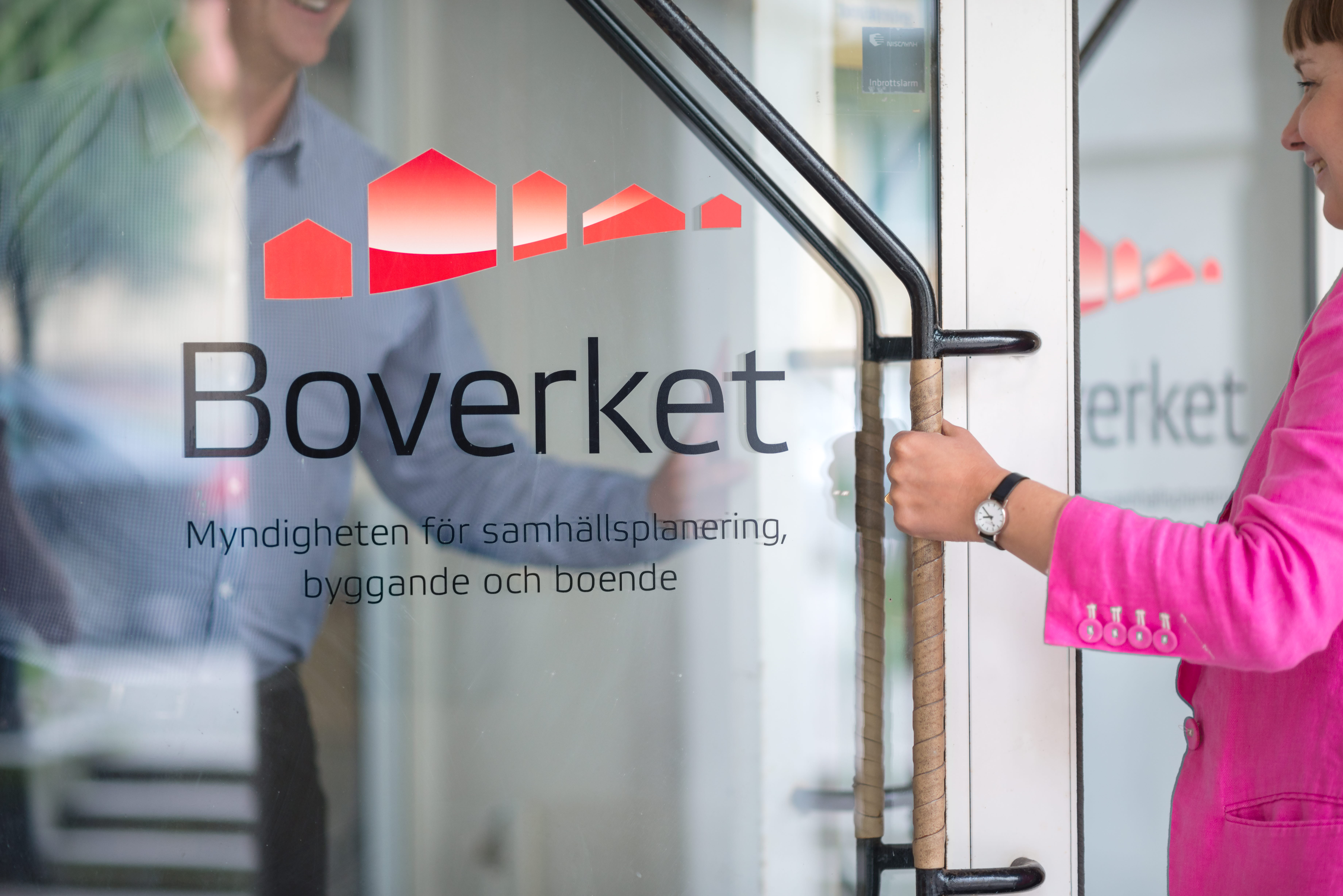 Kvinna öppnar glasdörr med Boverkets logotype