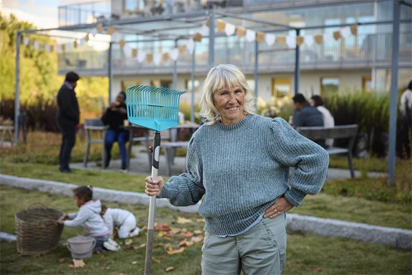 En person med en räfsa på en innergård i ett bostadsområde.
