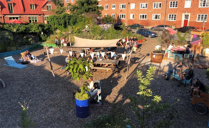 Foto som visar en innergård vid flerbostadshus med växter, solstolar och soltak.