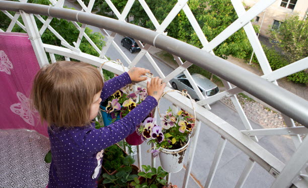 Liten flicka står på balkong och tittar på blommor.