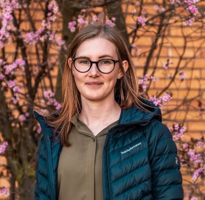 Thérese, med glasögon och utslaget hår står framför en blommande buske.