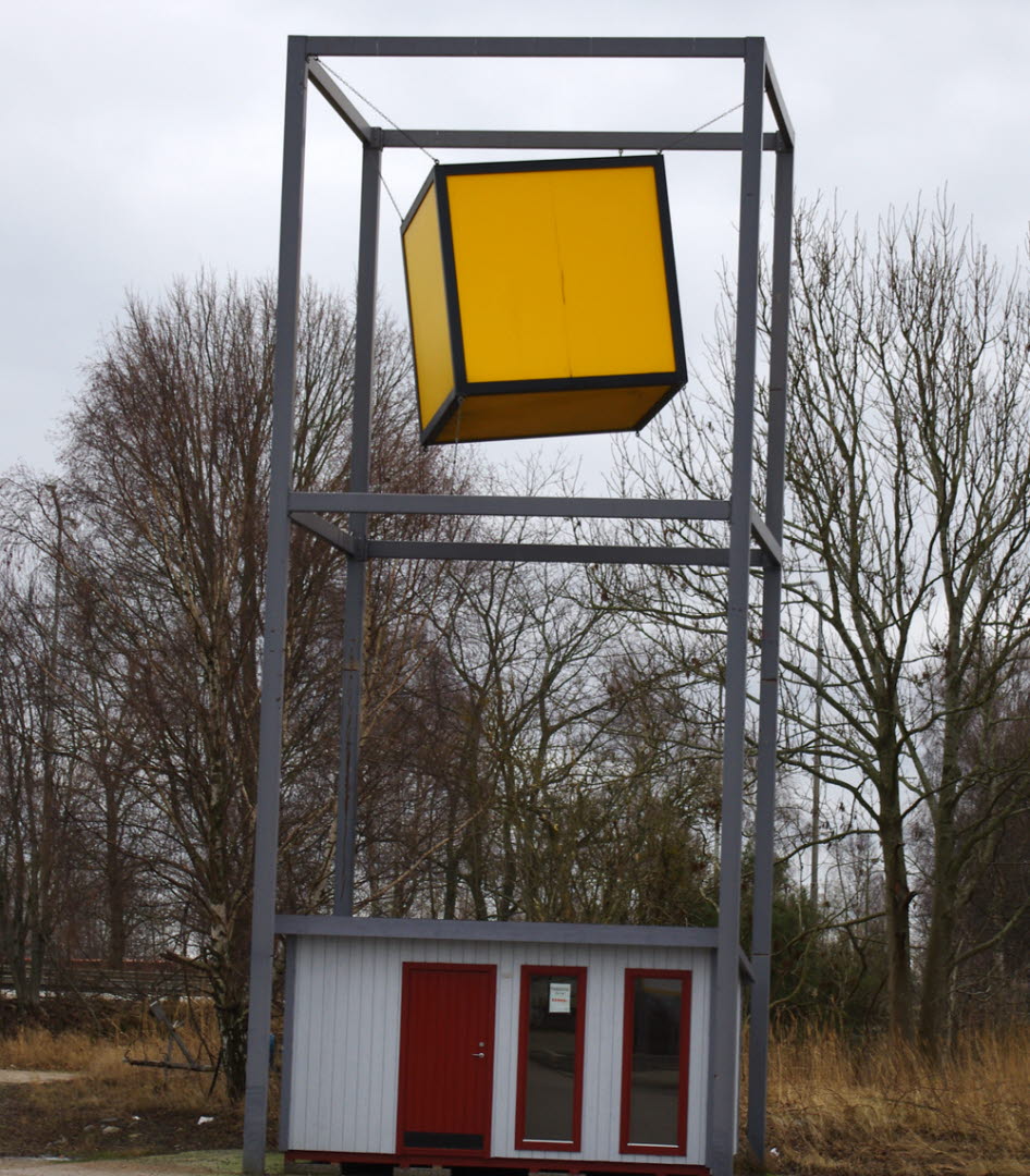 Foto på en konstruktion som består av en ram i grå metall och i mitten svävar en stor gul kub.