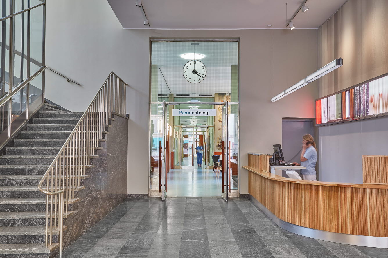 Trapphus med stengolv och en stor reception klädd i trä.