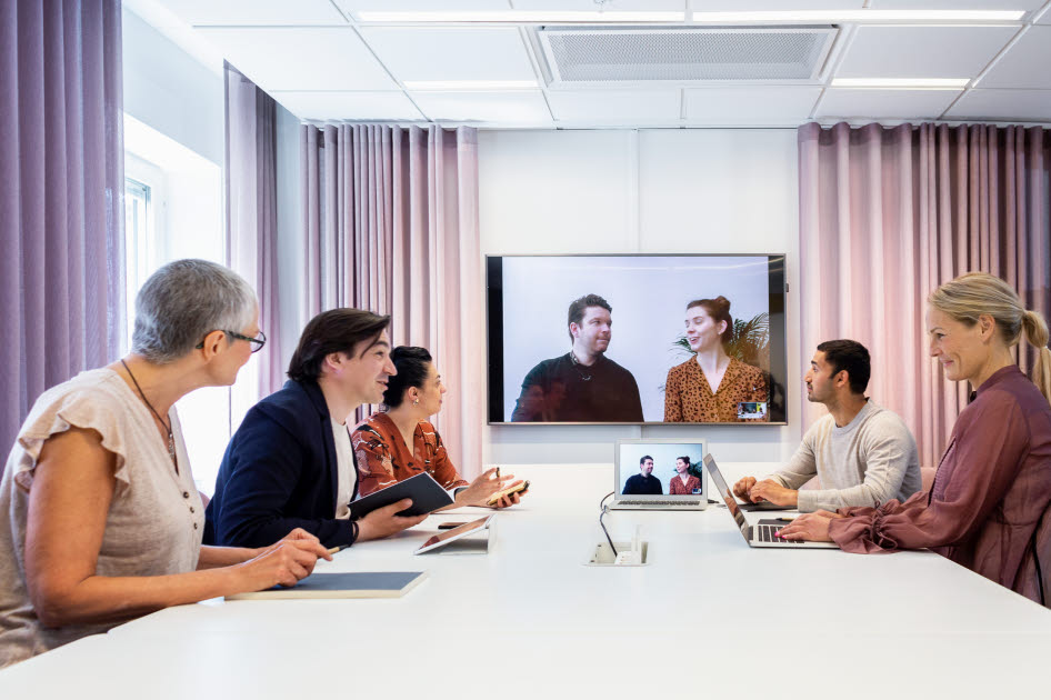Personer som sitter runt ett bord framför en digital skärm.