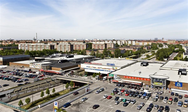 Flygbild över stadsmiljö med köpcentrum , viadukt samt flerfamiljshus .