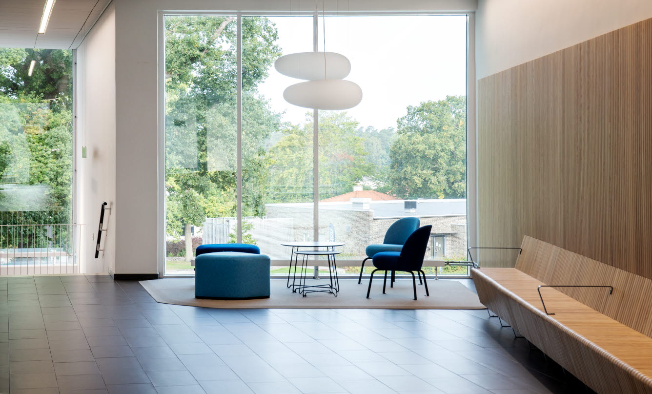 Väntrum med grönblå stoppade möbler med stora fönsterpartier som gör rummet ljust och luftigt.