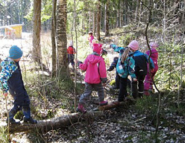 Barn i färgglada kläder på skogpromenad på en stock.