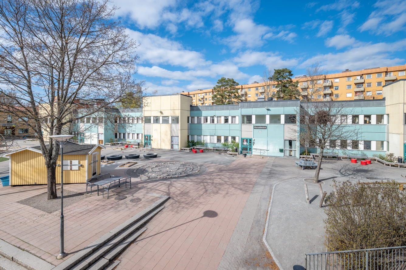 Foto på låg skolbyggnad med blå fasad. 