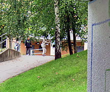 Två personer befinner sig vid ett hus ovanför en backe i ett bostadsområde. Foto: