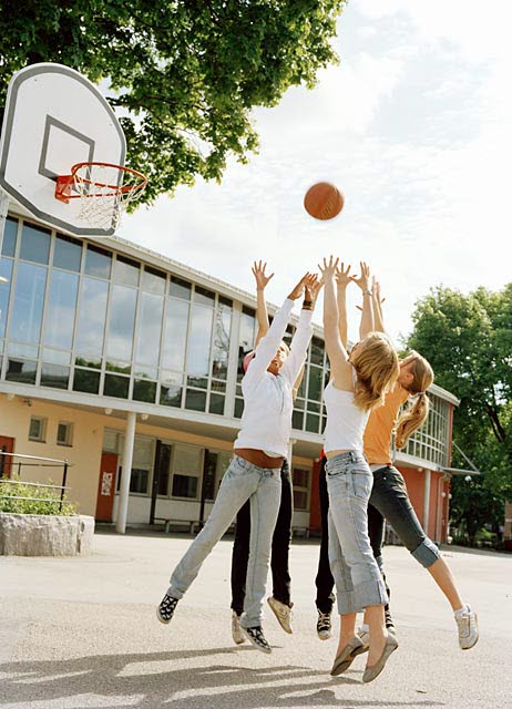 Foto på ungdomar som spelar basket på en skolgård.