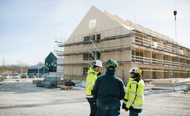 Tre personer står framför ett husbygge. Foto: