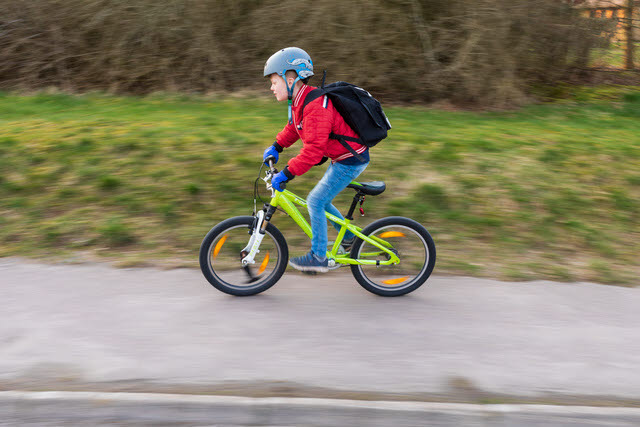 Barn i röd tröja som cyklar på en grön cykel.