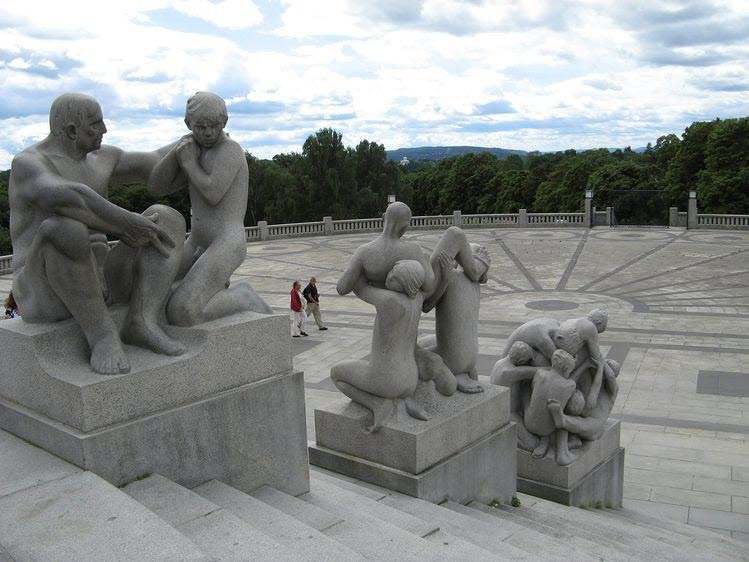Tre uppsättningar skulpturer av människor i betong som står på plattformar vid en stentrappa.