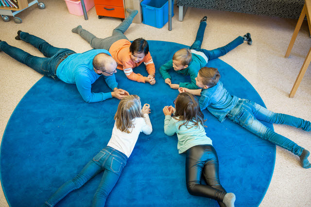 Sex barn ligger på mage på en stor rund blå matta.