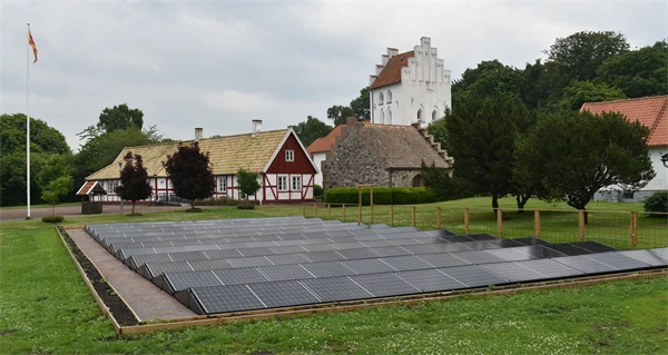 Solpaneler på en gräsmatta framför ett bostadshus och en kyrka.