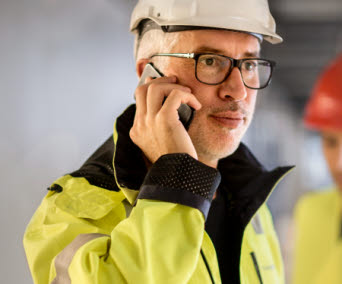 En man i varseljacka och arbetskläder talar i mobiltelefon. Foto: Scandinav/Plattform.