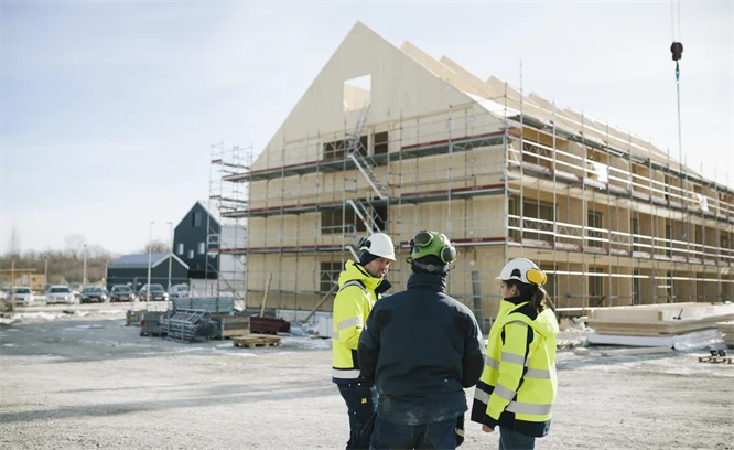 Tre personer står framför ett husbygge. Foto: