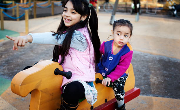 Två flickor som sitter på en gunghäst i en lekpark.