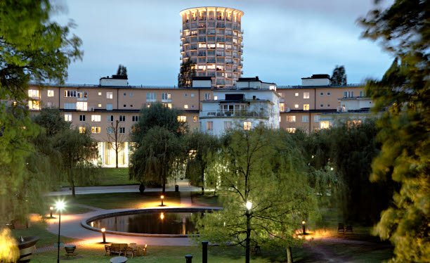 Flerbostadshus med en park i fonden. Belysning och damm i parken.