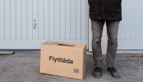 Flyttlåda och en person står på gatan. Bara benen syns. Foto.