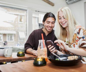 Två ungdomar umgås på café och tittar på en smartphone.