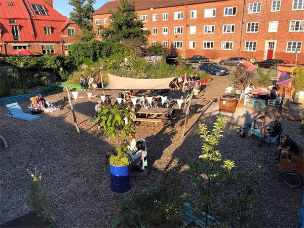 Foto som visar en innergård vid flerbostadshus med växter, solstolar och soltak.
