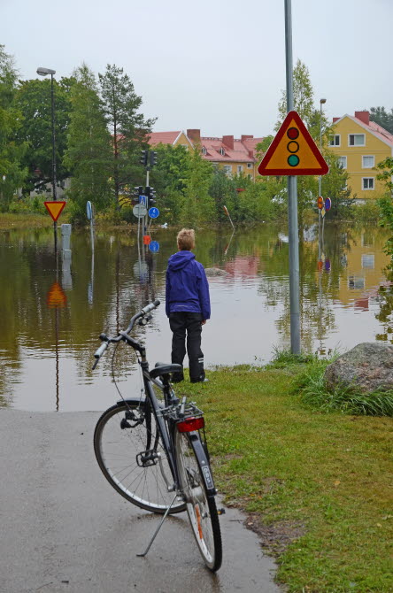 Ett barn har stigit av sin cykel vid översvämmad väg.