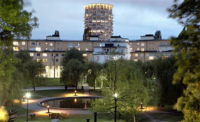 Flerbostadshus med en park i fonden. Belysning och damm i parken.