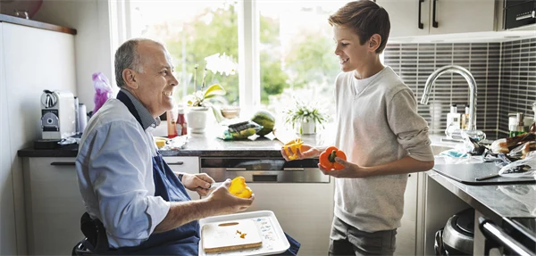 Pappa och son lagar mat i köket. Pappan använder rullstol. De är glada.