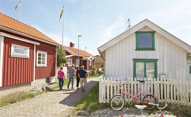 Fyra personer vandrar längs kullerstensgator i en kulturmiljö bland röda och vita trähus. Foto: Anders Järkendal/Scandinav