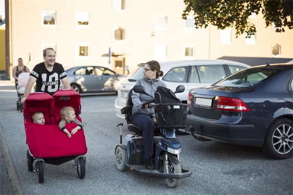 Person i permobil som kör brevid en annan person som kör en röd tvillingvagn.