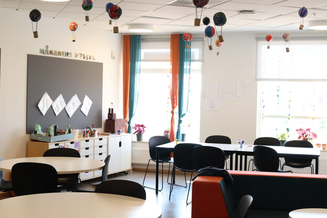 Foto på ett tomt klassrum med 15 små luftballonger som hänger i taket