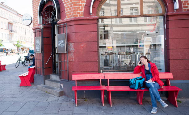 Kvinna som sitter på bänk utanför skyltfönster och pratar i telefon. Foto: Peter Kroon