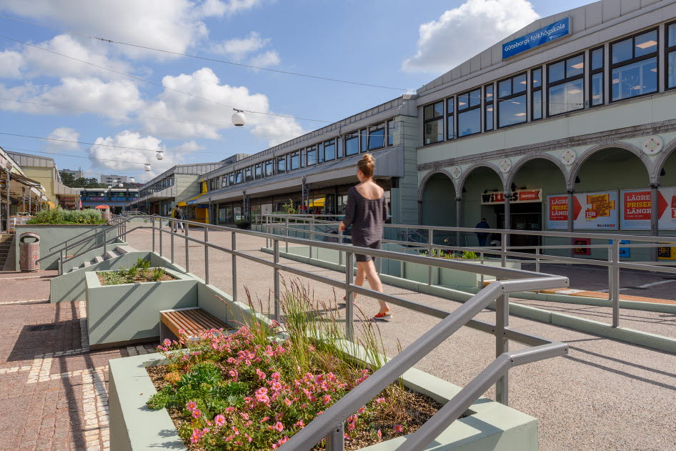 Bilden visar trivsel- och trygghetsskapande fysiska åtgärder på Vårväderstorget i Göteborg i form av en lång ramp kantad av planteringar, sittmöbler och ny markbeläggning. En yngre kvinna syns mitt i bilden.