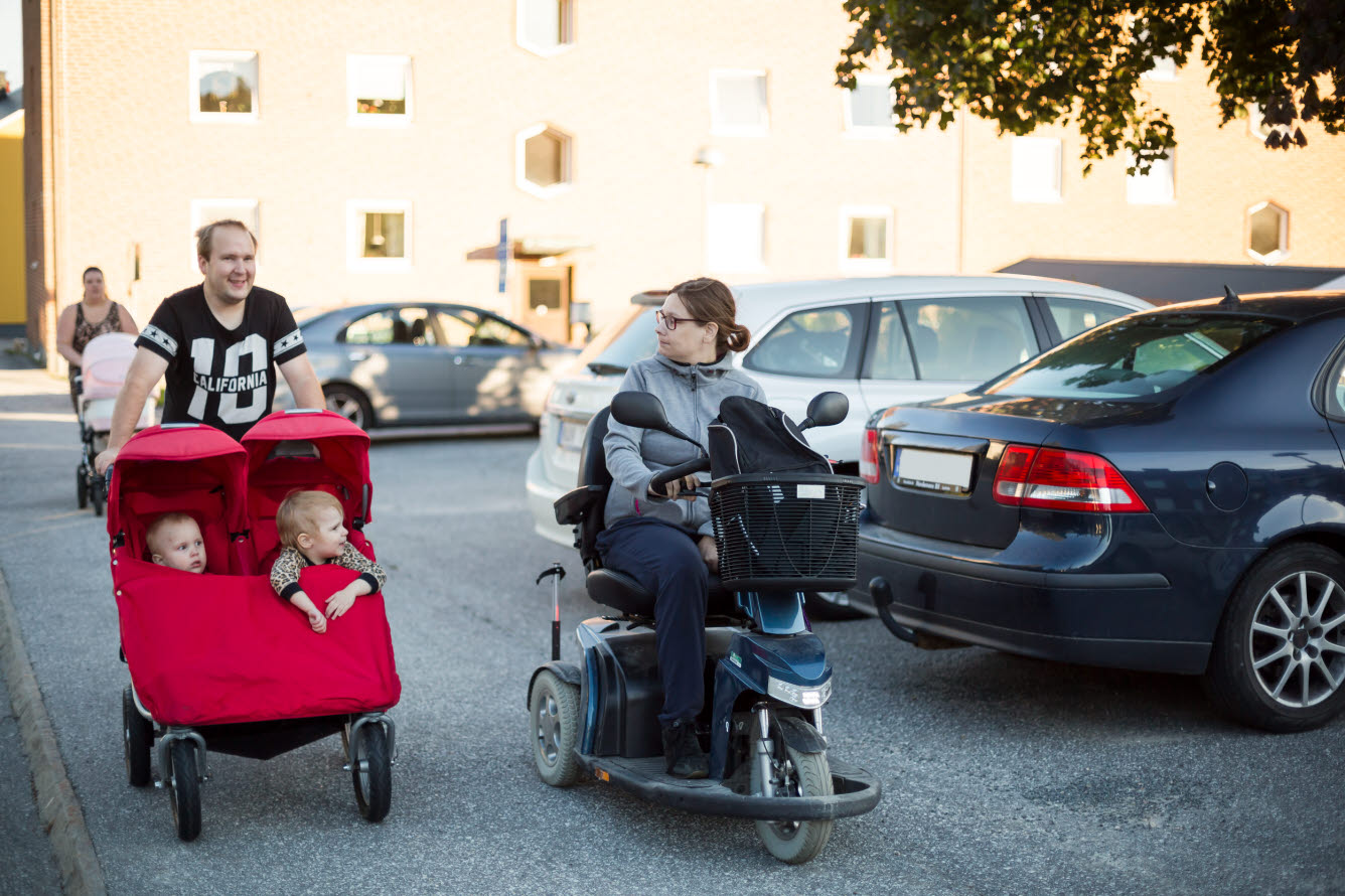 Person i permobil som kör brevid en annan person som kör en röd tvillingvagn.