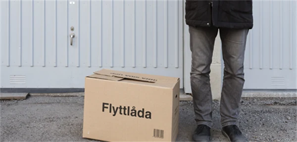 Flyttlåda och en person står på gatan. Bara benen syns. Foto.